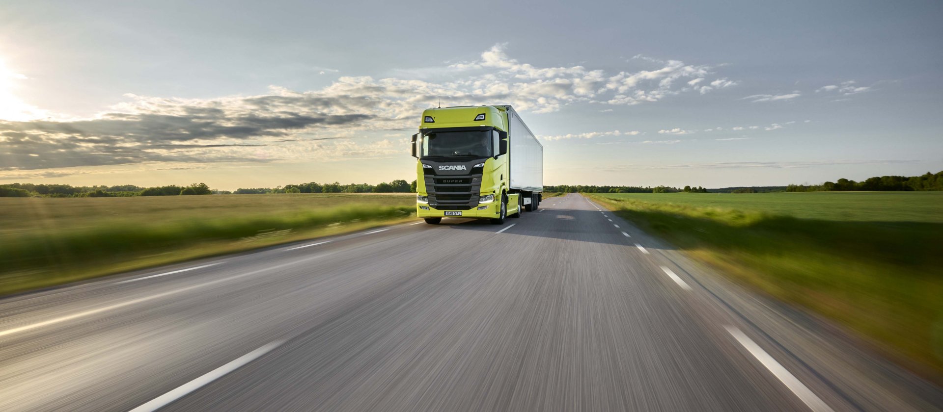 Ein gelber Scania-LKW auf einer von grünen Feldern umgebenen Straße